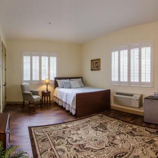 A cozy bedroom with a large bed, ornate rug, and natural light from windows.