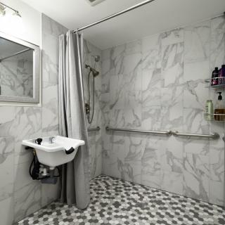 An accessible bathroom with marble tiles, featuring a shower area with a curtain and grab bars for support.