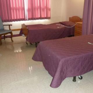 An empty room with two twin beds, purple bedding, and a chair by the window.