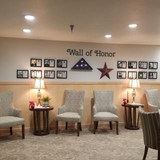 A 'Wall of Honor' displays framed photographs and patriotic decorations, accompanied by a row of chairs and lamps in a warmly lit room.