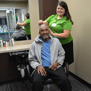 A cheerful hairstylist provides a haircut to an elderly man in a salon setting.