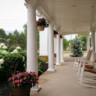 A serene porch with white columns, rocking chairs, and vibrant flower arrangements.
