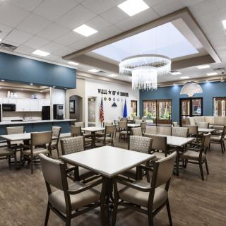 A spacious and modern dining area with tables and chairs, featuring a large chandelier and ceiling lights.