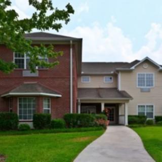 A two-story residential building with a well-maintained lawn and a concrete pathway leading to the entrance.