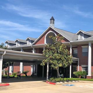 A brick building with white columns and a covered entrance on a sunny day.