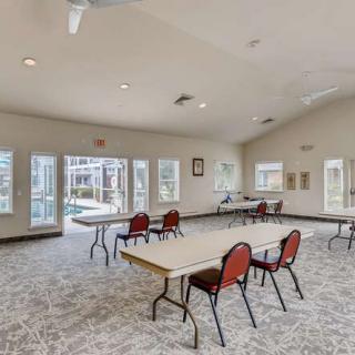 A spacious community room with tables and chairs, well-lit by natural light through large windows.