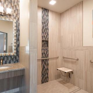 A modern, accessible bathroom with a walk-in shower featuring a foldable bench and grab bars.