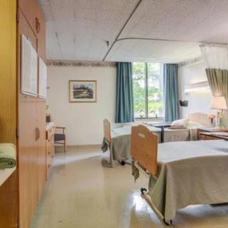 A shared hospital room with two beds, equipped with essential furniture and a window providing natural light.