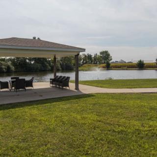 A scenic view of a gazebo overlooking a calm lake with patio furniture on a sunny day.