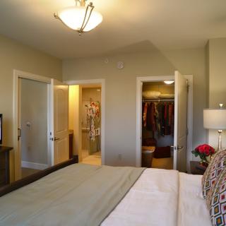 A cozy bedroom with a neatly made bed, television, and an open closet.