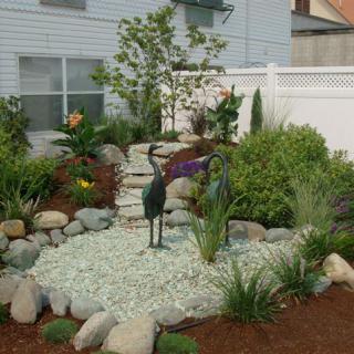 A beautifully landscaped garden featuring stones, lush plants, and decorative bird sculptures.