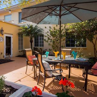 A sunny patio with outdoor seating and an umbrella, surrounded by plants and flowers.