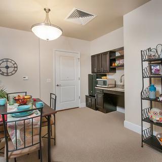 A small dining area with a table set for a meal, adjacent to a kitchen space featuring shelves and a microwave.