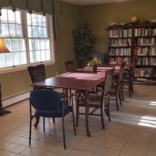 A cozy dining area featuring a wooden table surrounded by various chairs, illuminated by natural light from the windows.