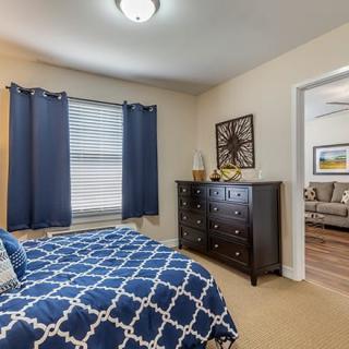 A cozy bedroom with blue curtains and a patterned bedspread, featuring a dark wood chest of drawers.