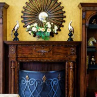 A beautifully decorated fireplace with a vintage wooden mantel, adorned with a decorative mirror and floral arrangement.