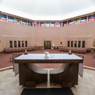 A modern chapel interior with a central altar and surrounding flags.