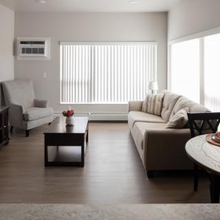 A minimalist living room featuring a sofa, armchair, and coffee table with large windows and vertical blinds.