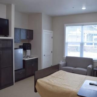 A cozy studio apartment with a bed, sofa, kitchenette, and TV.