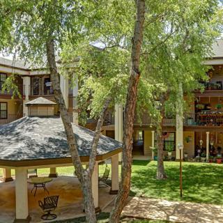 A peaceful courtyard featuring a gazebo surrounded by lush trees and a multi-story building.