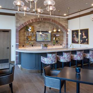 A modern bar area featuring a curved counter with stylish seating, chic chandeliers, and artwork on the walls.