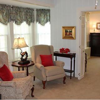 A cozy living room with armchairs, a lamp, and decorative pillows against a backdrop of large windows with curtains.