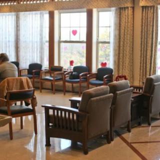 A quiet waiting room with several chairs arranged near large windows letting in daylight.