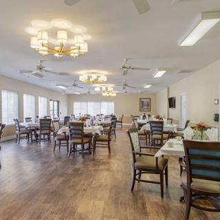 A spacious dining area with neatly arranged tables and chairs, featuring elegant lighting fixtures and wooden flooring.