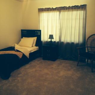 A simple bedroom with a single bed, nightstand, and chair.