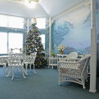 A cozy room decorated for the holidays with a Christmas tree, wicker furniture, and a large mural.