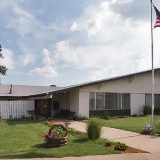 A single-story building with a flagpole and neatly landscaped grounds under a cloudy sky.