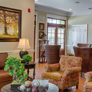 A cozy living room with armchairs, a coffee table with plants, and a painting on the wall.