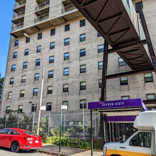 A view of an apartment building with a connecting walkway, featuring a red car parked in front.