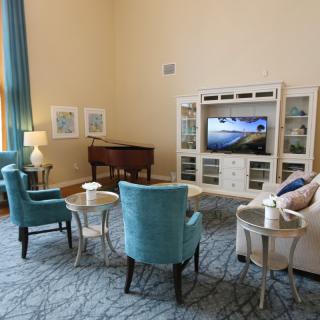 A cozy living room with elegant furniture, featuring a television, blue chairs, a couch, and a piano.