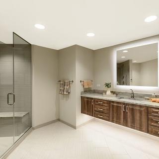 A modern bathroom featuring a glass shower, wooden vanity, and illuminated mirror.