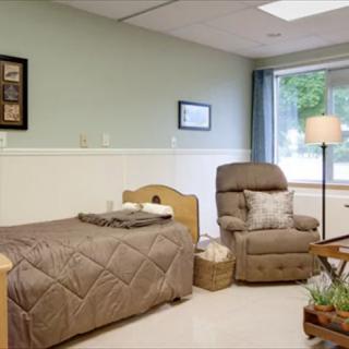 A cozy bedroom with a bed, recliner, and floor lamp next to a window.