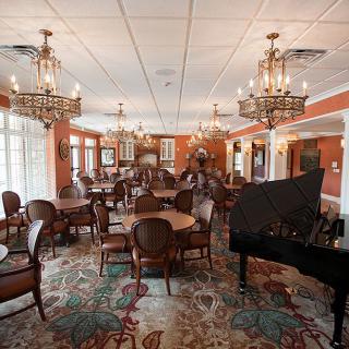 A luxurious dining room with chandeliers, elegant seating, and a grand piano.
