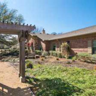 A beautiful garden with a pergola in front of a brick house on a sunny day.