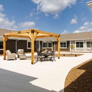 A spacious outdoor courtyard with a wooden pergola and comfortable seating under a clear blue sky.
