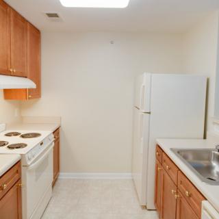 A compact apartment kitchen with wooden cabinets and white appliances.