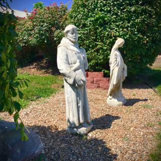 Two statues stand in a serene garden setting, surrounded by lush greenery.