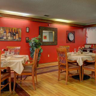 A cozy restaurant dining area with red walls, elegantly set tables, and wooden chairs on a polished floor.
