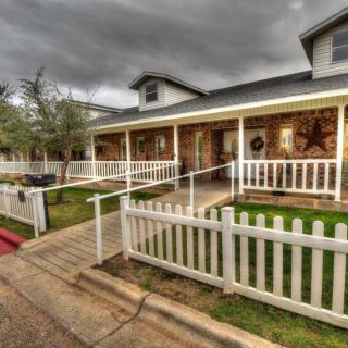 A suburban house with a porch, white picket fence, and a neatly maintained yard under a cloudy sky.