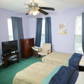 A cozy bedroom with two twin beds, a television, ceiling fan, and seating area.
