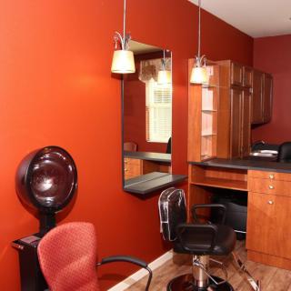 A bright salon interior with red walls, chairs, a mirror, and hair styling equipment.