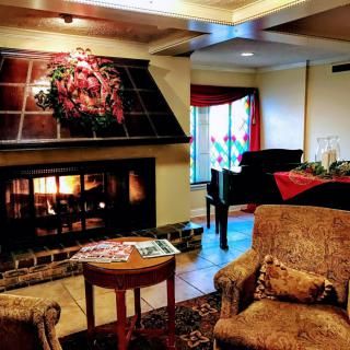 A cozy living room featuring a warm fireplace, elegant piano, and comfortable seating arranged with tasteful decor.