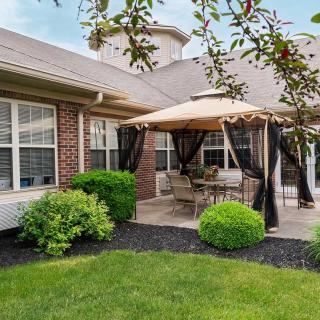 A cozy patio area with a gazebo and outdoor seating, surrounded by well-maintained landscaping next to a brick building.