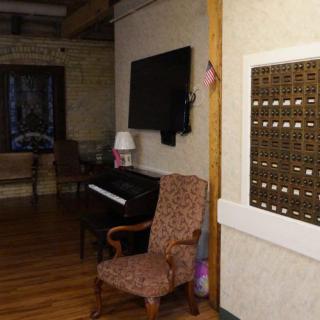 An interior room featuring a piano, armchair, wall-mounted TV, and a set of mailboxes.