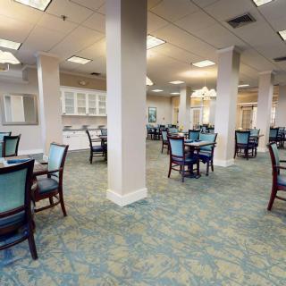 A spacious dining area with multiple tables and chairs, featuring a carpeted floor and overhead lighting.