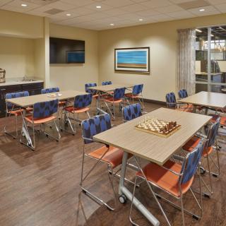 A modern conference room with tables, chairs, and a television on the wall.